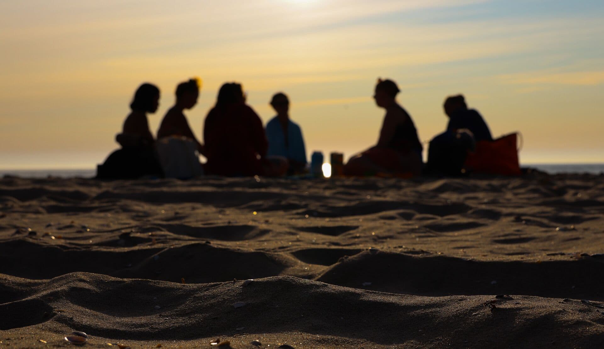 Silhouet van een groep mensen bijeen op het strand bij zonsondergang.